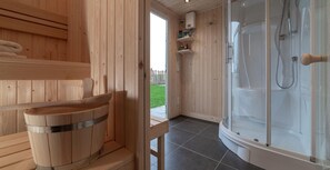 Et sauna-rum i træ med en træspand, et bruseområde med glasvægge og udsigt til en grøn græsplæne.