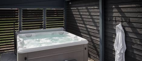 A hot tub with a bench and a towel rack against a wooden wall.