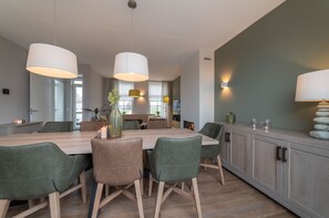 Ein moderner Essbereich mit Holztisch, grünen Sitzstühlen und Pendelleuchten.