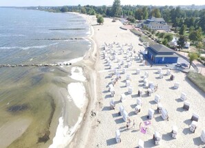 Une plage bordée de rangées de chaises longues blanches et un bâtiment bleu doté d’un toit en pente.