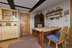 A wooden dining table with chairs, a wooden cabinet with glass doors, and a shelf with ceramic mugs. - Attractive Holiday Home in Ahlbeck With Terrace (Ahlbeck)