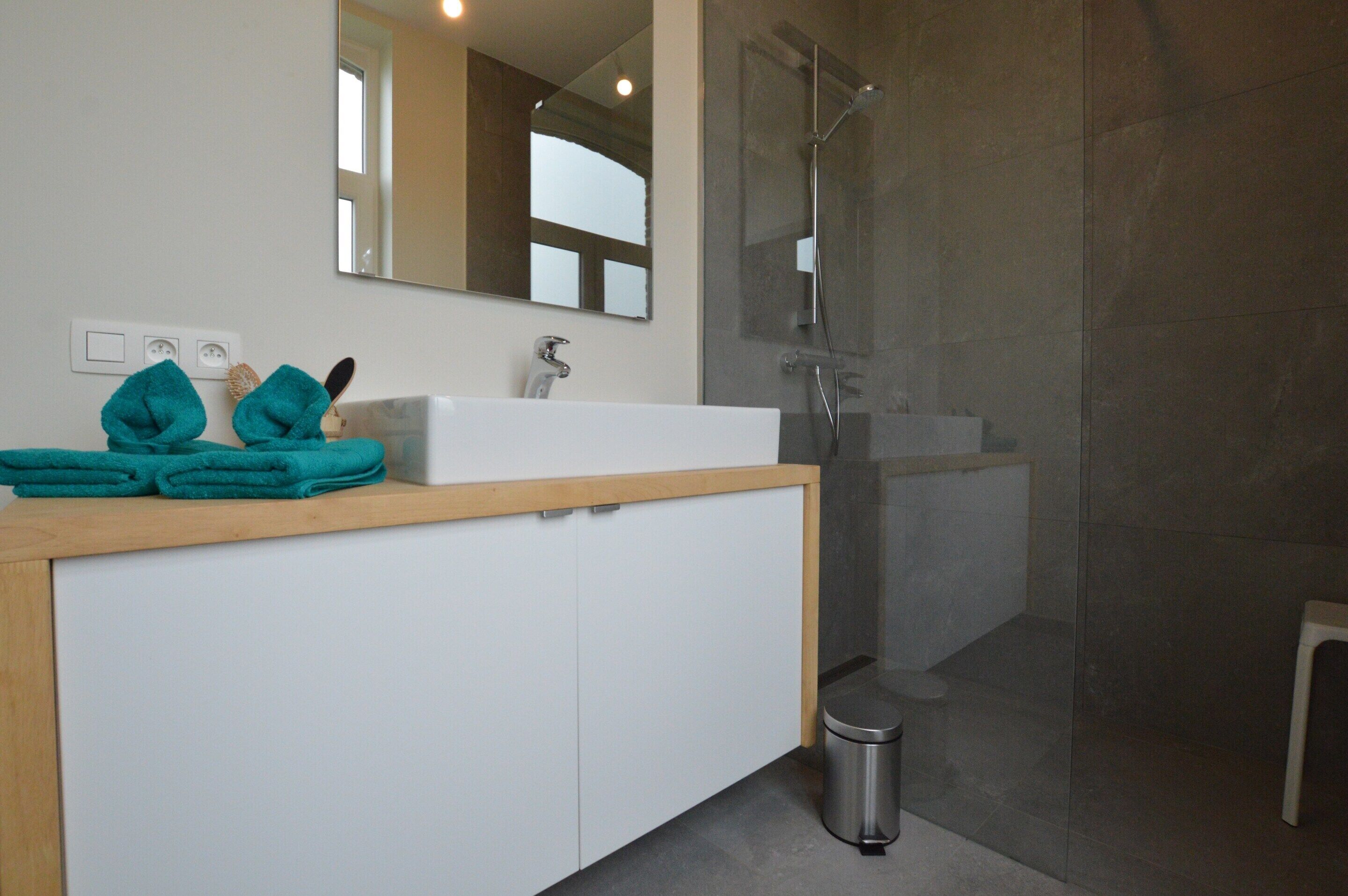 Une salle de bain moderne avec un meuble-lavabo blanc, un grand miroir et une douche à parois de verre.