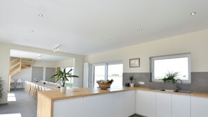 A modern kitchen with a wooden island, white cabinets, and large windows providing natural light.