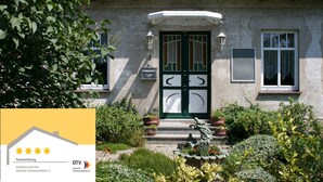 A house with a red-tiled roof, a green door, and a small garden with potted plants. - Landhauswohnung in Kroepelin mit Grossem Garten (Kroepelin)