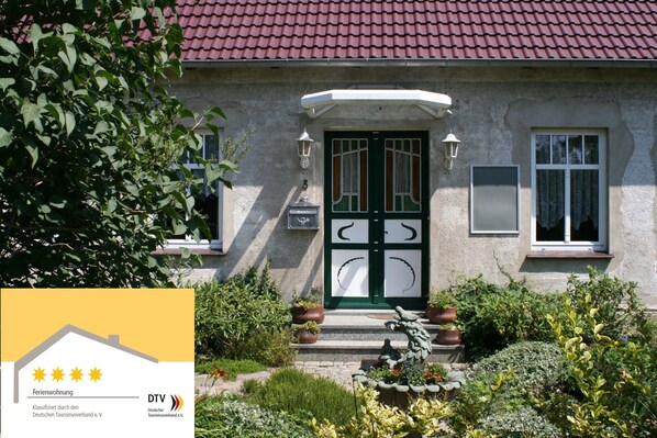 Una casa con tetto in tegole rosse, una porta verde e un piccolo giardino con piante in vaso.