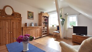 Une pièce comprenant un meuble en bois, une télévision, une chaise et une fenêtre avec des rideaux.