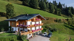 A two-story chalet with a balcony, a covered porch, and a car parked in front. - Apartment in Sankt Johann im Pongau Near Ski Area (Sankt Johann im Pongau)