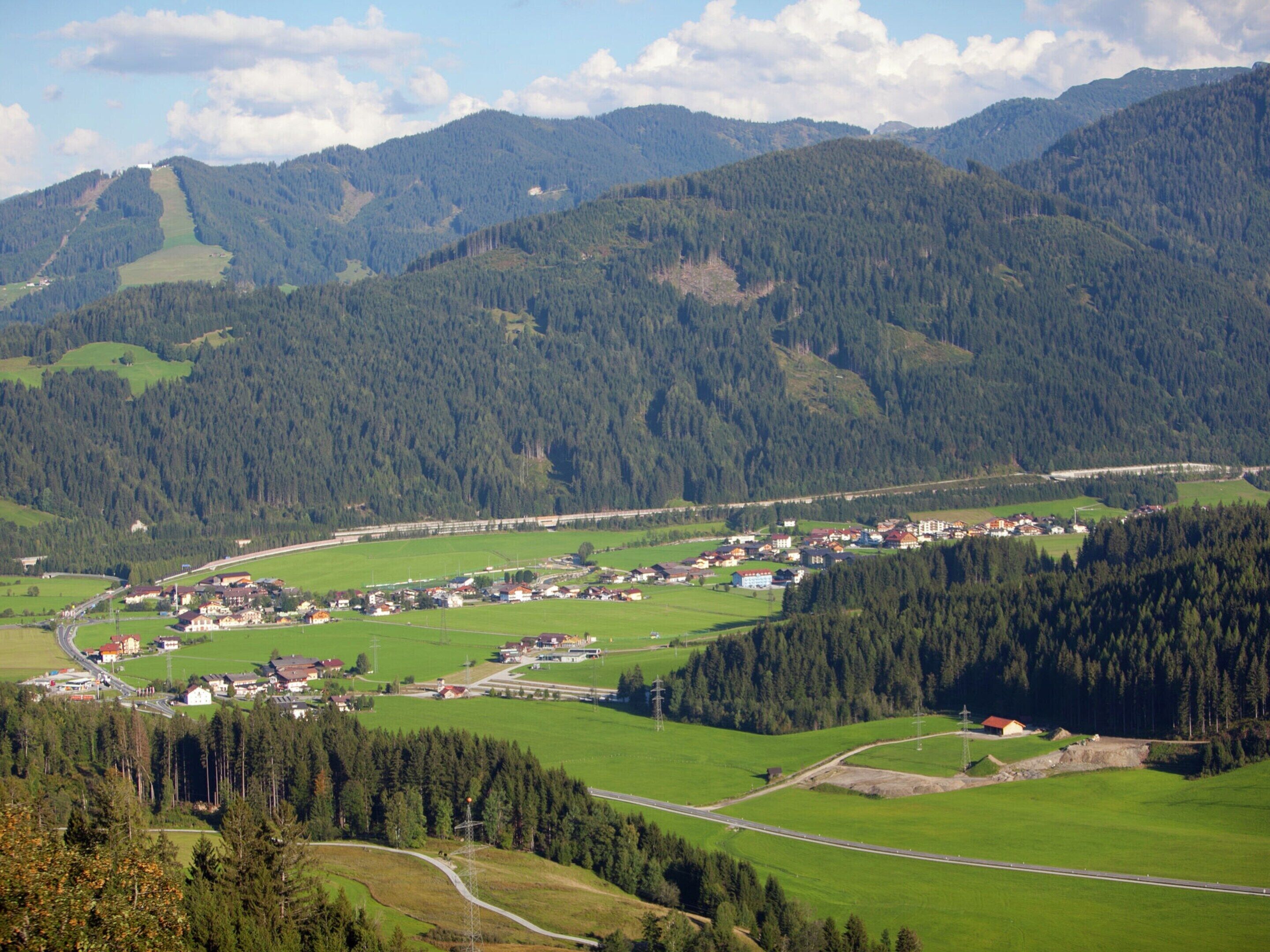 A rural landscape with a small village nestled among green hills and forests.