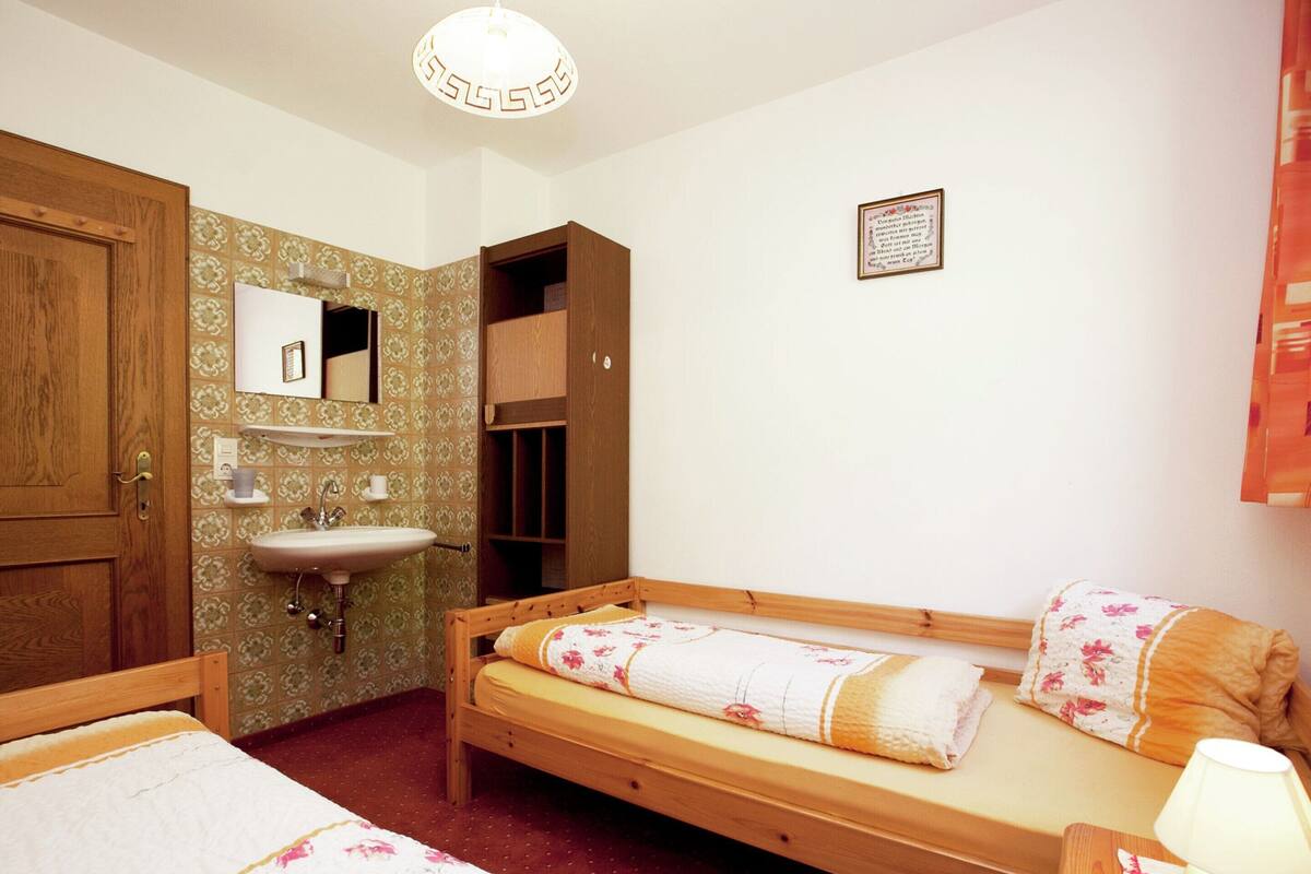 Ein Schlafzimmer mit zwei Einzelbetten, einem Holzschrank, einem Nachttisch mit Lampe, einem Spiegel und einem Wandregal.