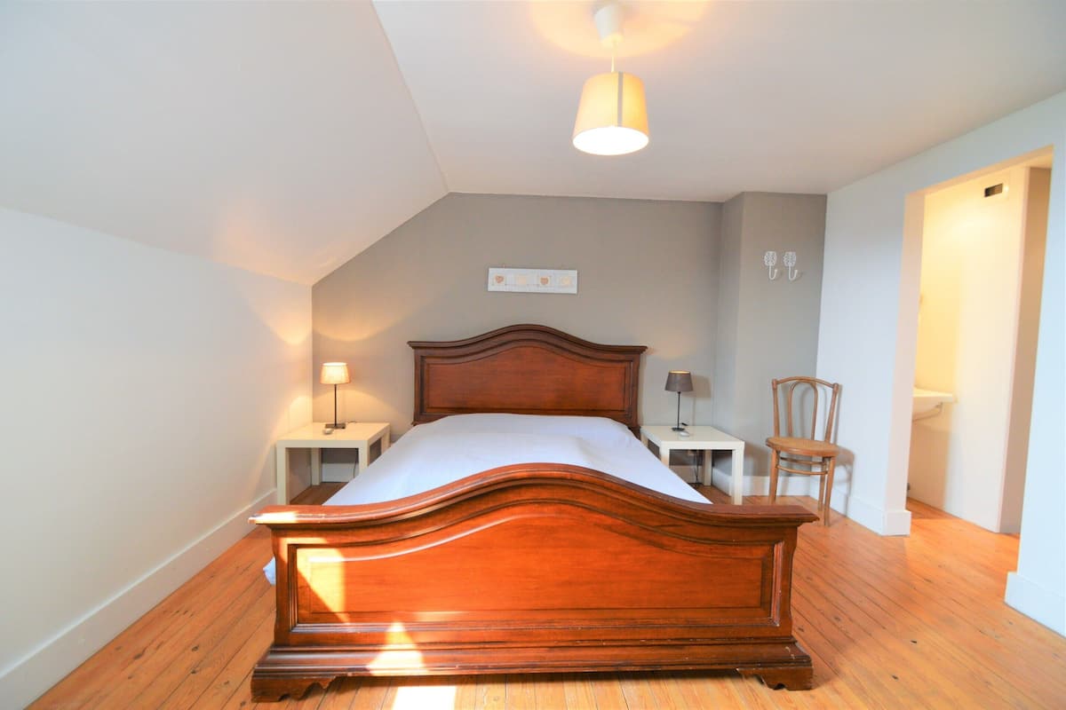 A bedroom with a wooden bed, two bedside tables with lamps, a chair, and a ceiling light.