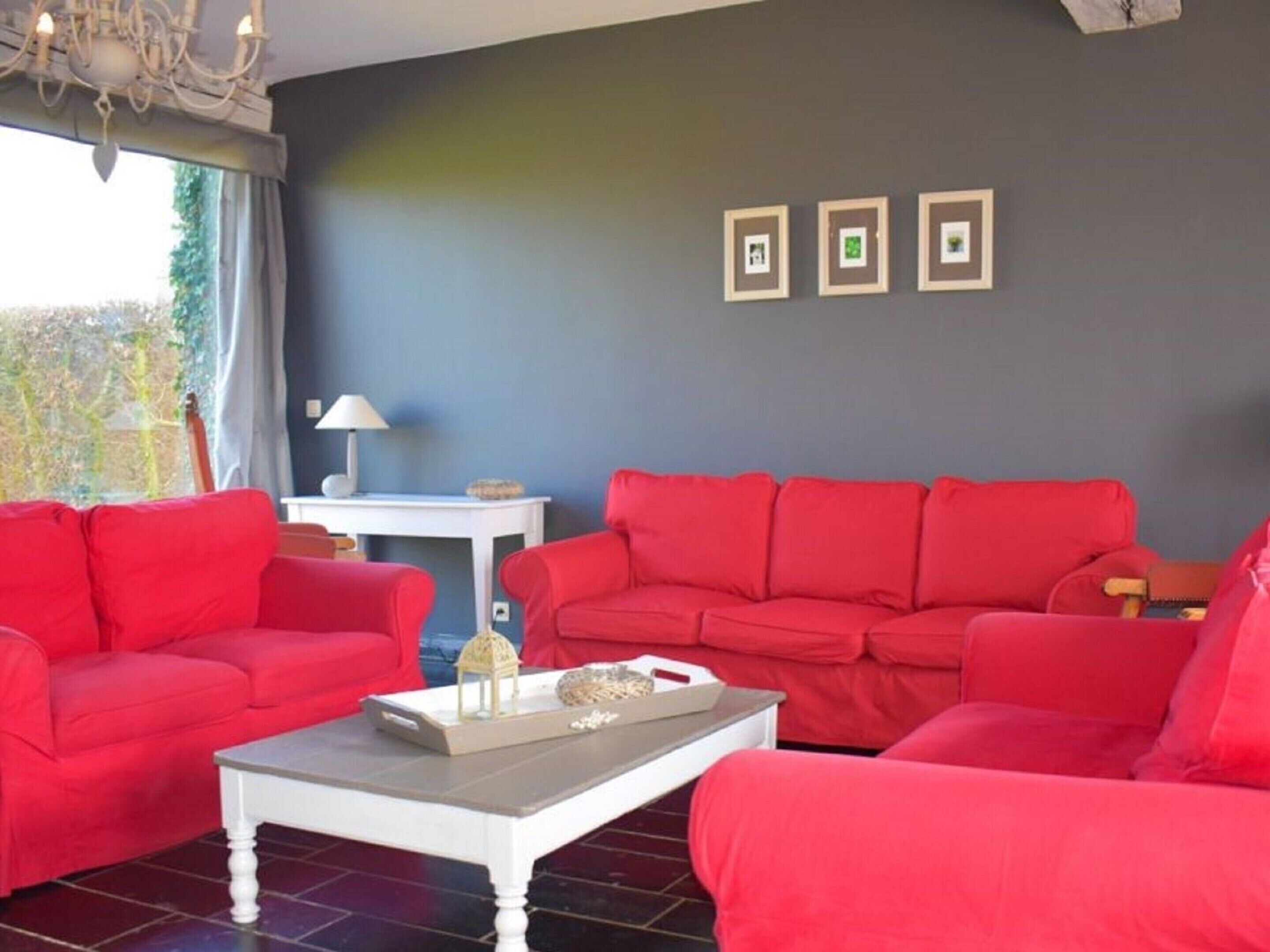A living room with red sofas, a white coffee table, and a small white table with a lamp. There are three framed pictures on the wall.