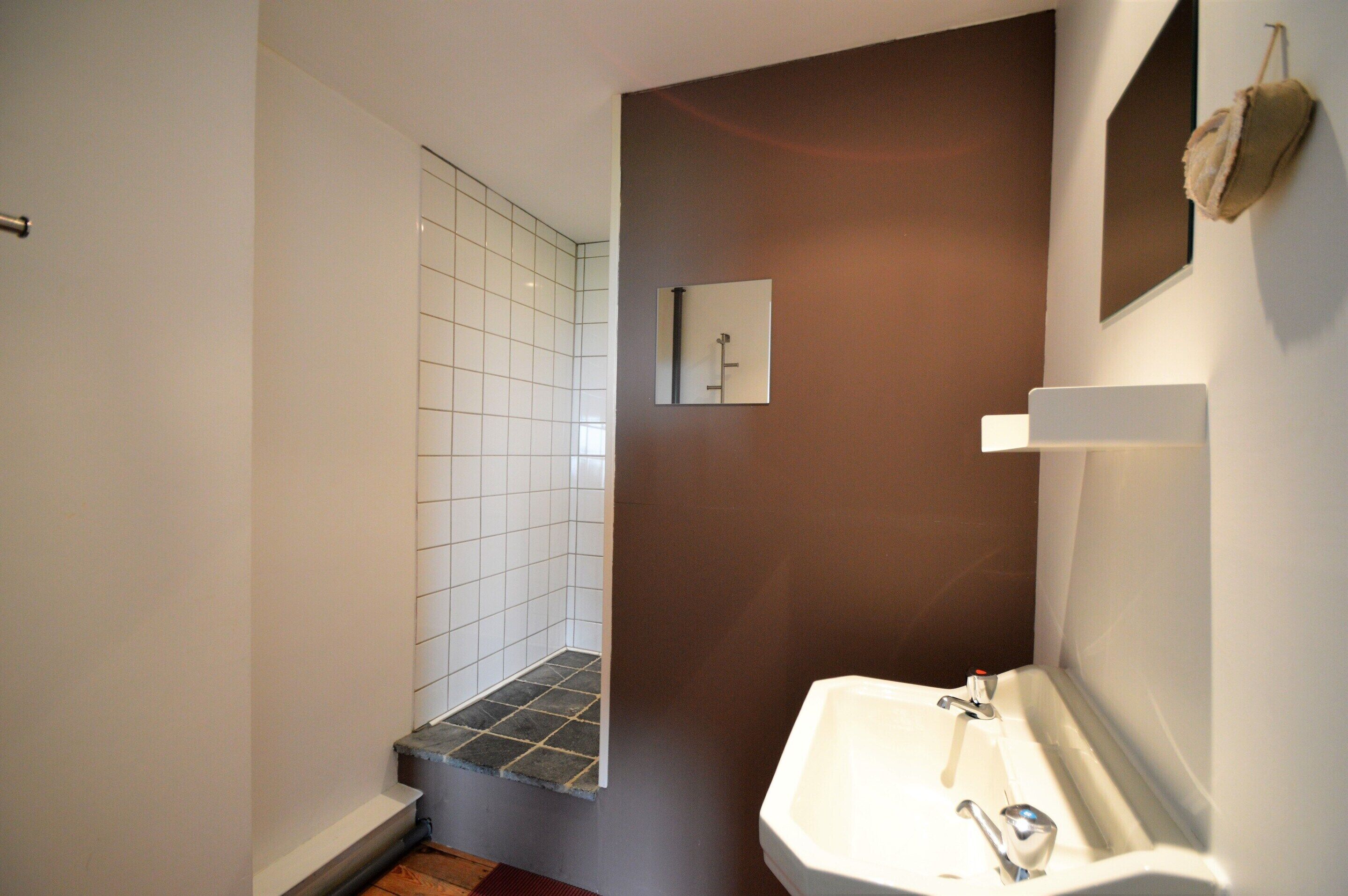 Un bagno con un lavandino bianco, uno specchio e uno spazio doccia con pareti piastrellate e un piccolo gradino.