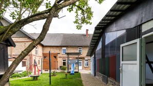 Une cour avec un bâtiment en briques, un arbre, une aire de jeux et un chemin pavé.