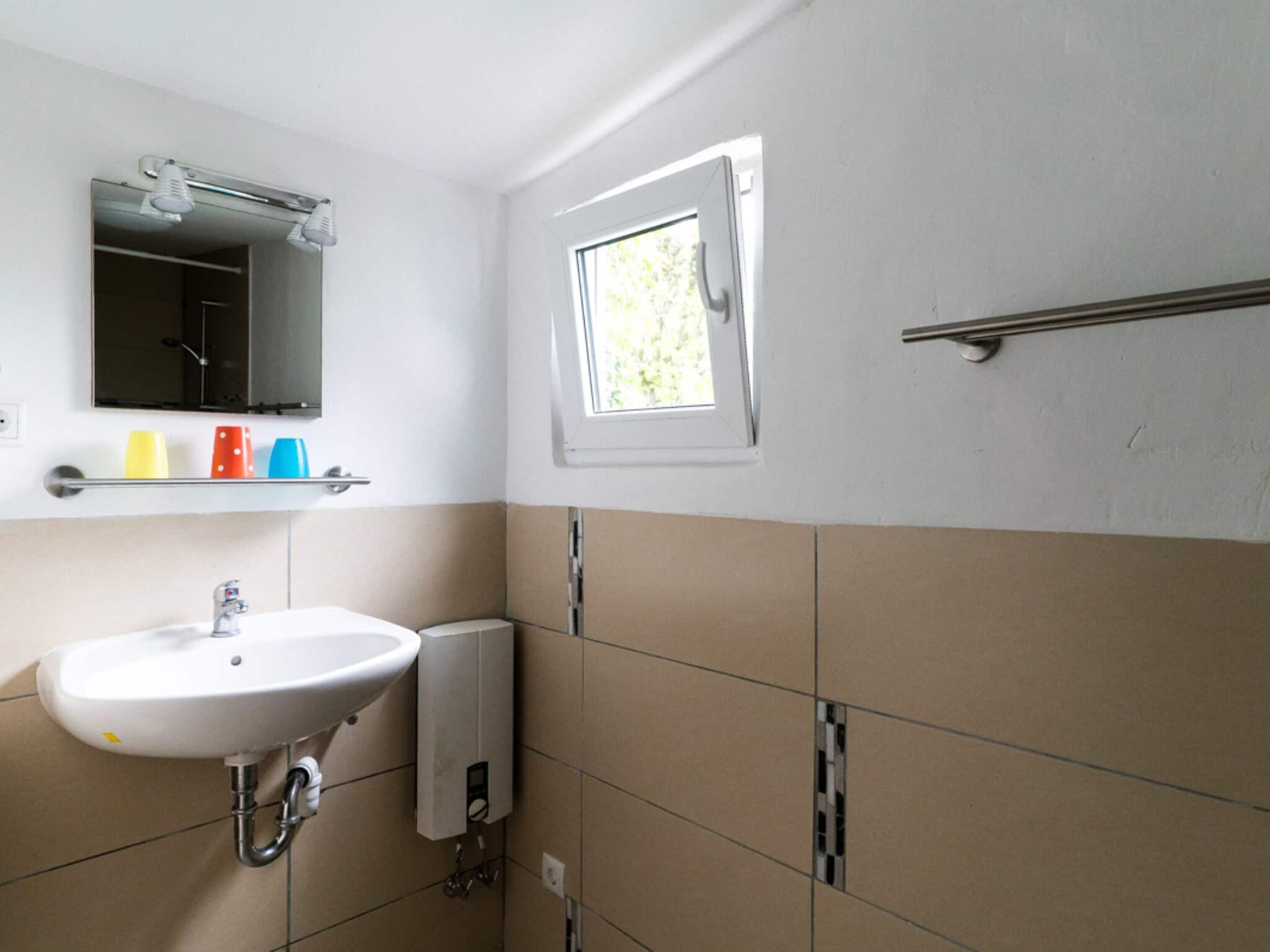 A bathroom with a white sink, a mirror, a window, and a towel rack.