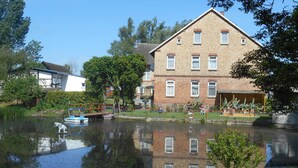 Un bâtiment en briques doté de nombreuses fenêtres, dont le reflet se mire dans l’eau.