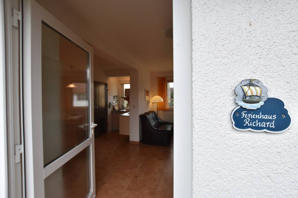 A hotel interior with a glass door entrance, a lounge area with a leather sofa, and a wall-mounted sign reading "Ferienhaus Richard".