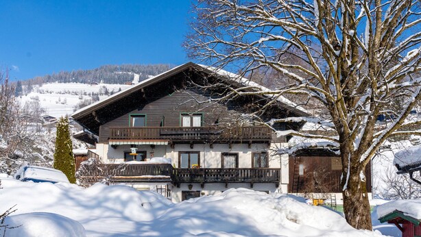 Eine zweistöckige Chalet mit Balkon, umgeben von schneebedecktem Gelände und Bäumen.