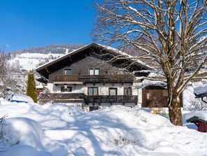 A two-story chalet with a balcony, surrounded by snow-covered ground and trees. - Cozy Apartment in Niedernsill Near Lake (Niedernsill)
