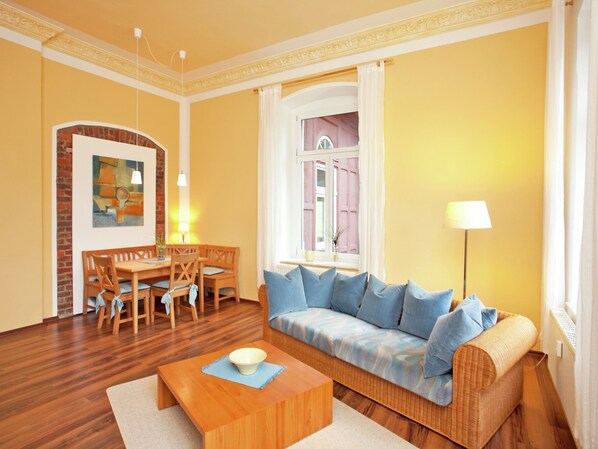 A living room with a wooden floor, a sofa with blue cushions, a dining table with chairs, and a painting on the wall. - Alluring Villa in Grunhainichen-borstendorf With Garden (Grünhainichen)