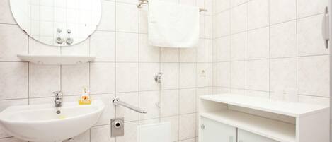 A modern bathroom with a white sink, round mirror, and a cabinet with a towel hanging above it.