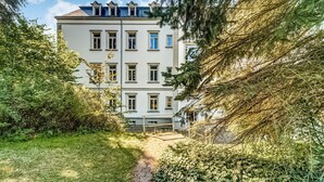 Un immeuble à plusieurs étages doté d’une entrée centrale, entouré d’une végétation luxuriante et d’un chemin pavé menant à l’entrée.