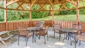 Une terrasse couverte avec des poutres en bois, des meubles en osier et une table en pierre.