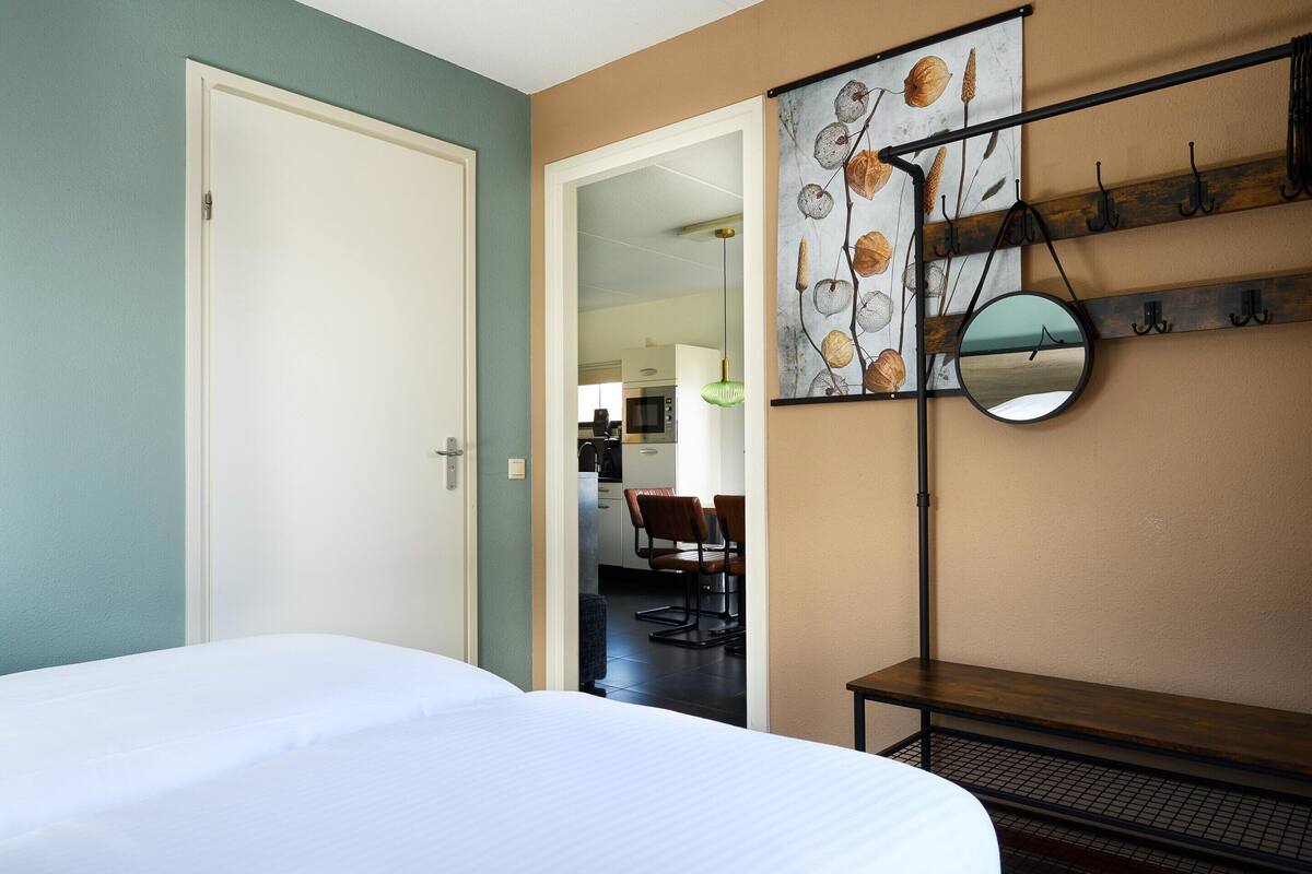 A hotel room with a bed, a dining area with chairs, and a wall-mounted mirror.