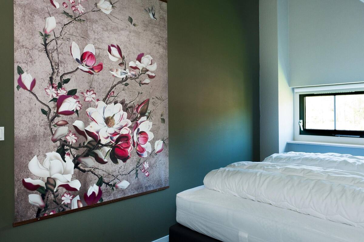 A bedroom with a large floral artwork on the wall, a bed with white bedding, and a window with daylight.