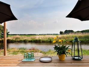 Une terrasse en bois offrant une vue sur une rivière, entourée de verdure et sous un ciel dégagé.
