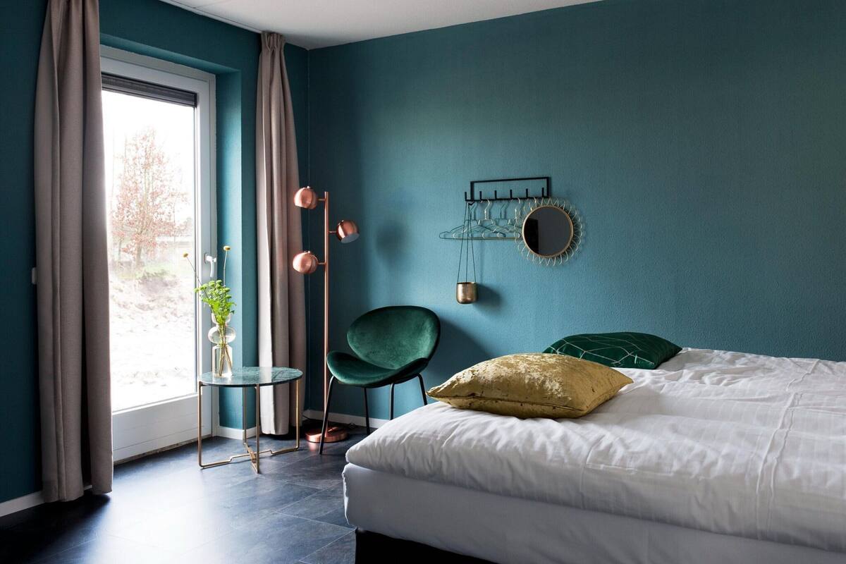 A bedroom with a bed, a chair, a table, and a window with curtains.