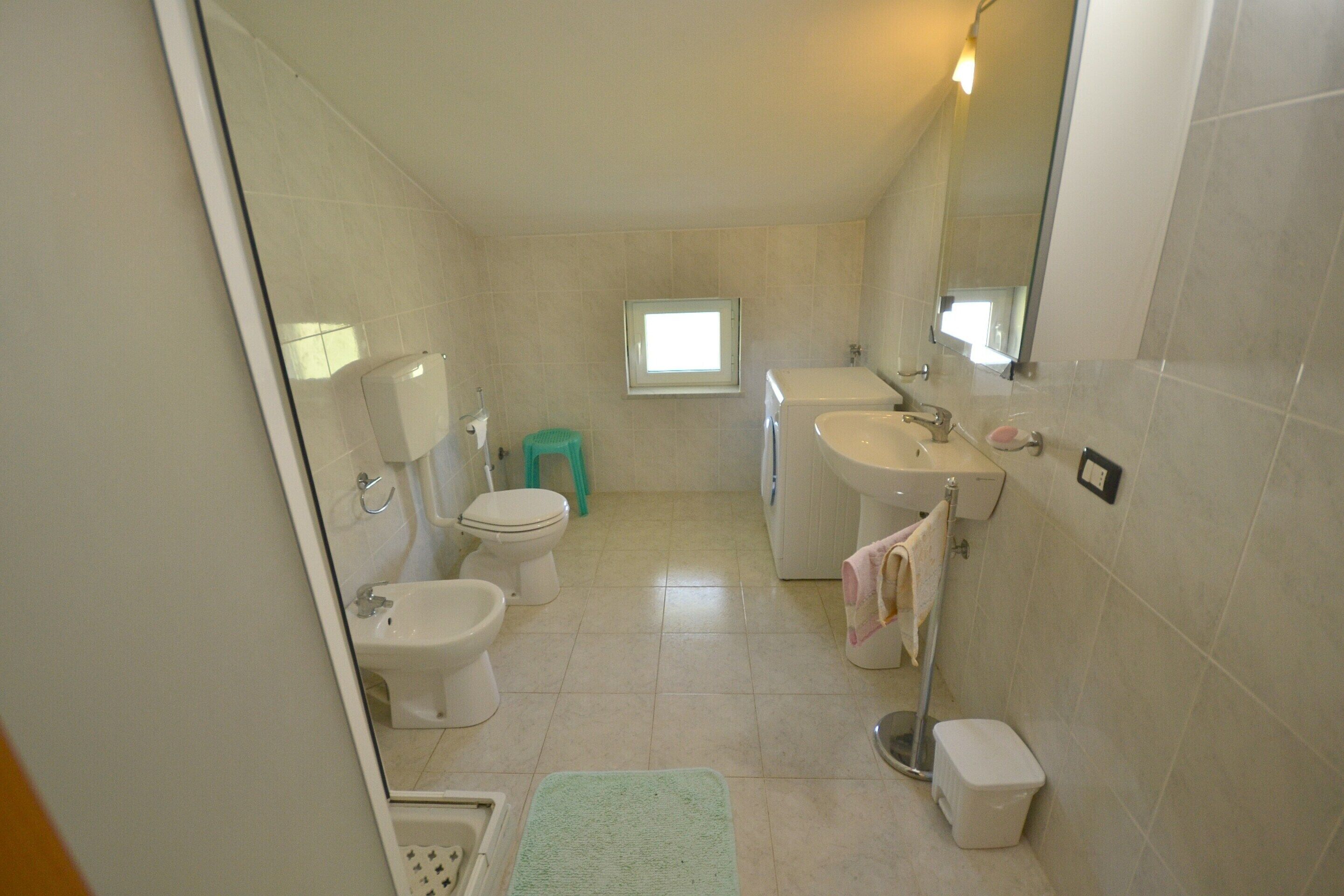 Un baño pequeño y limpio con inodoro, bidé, lavamanos y ventana.