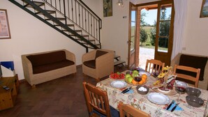 A dining area with a table set for four, surrounded by wooden chairs. A staircase is visible to the left, leading to an upper floor.