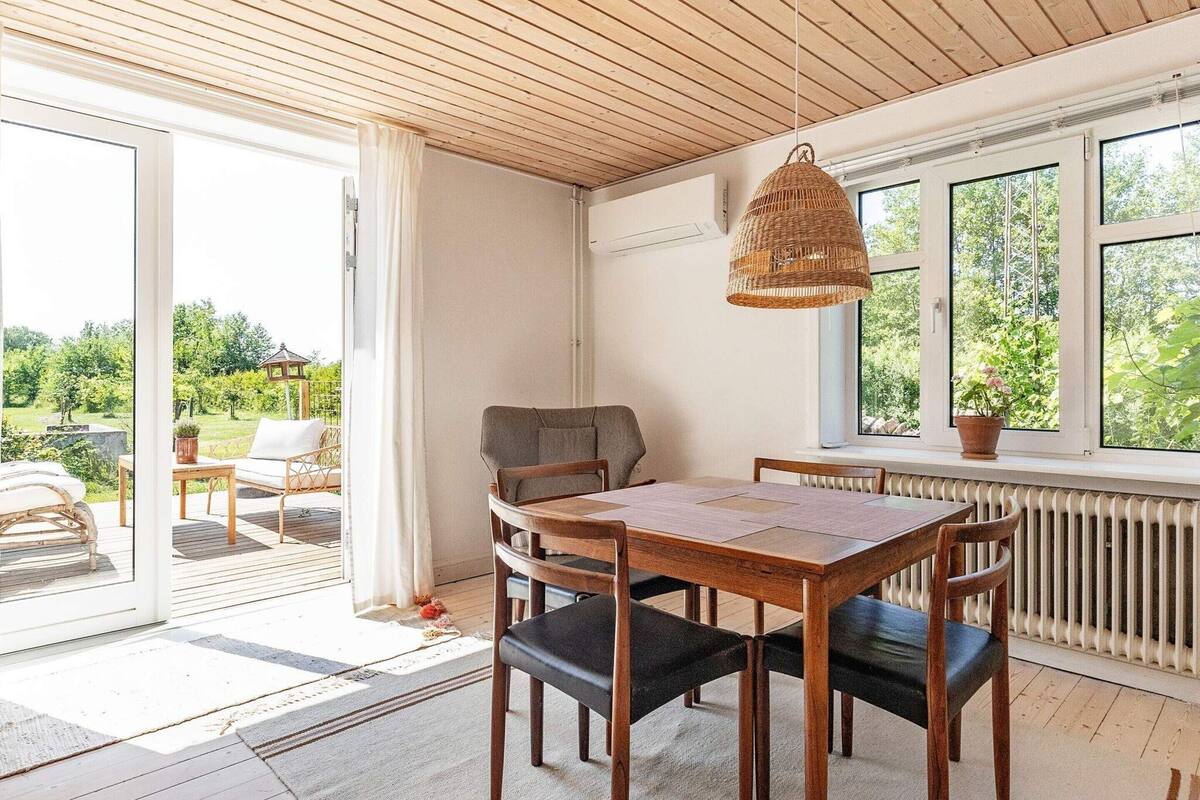 Comedor con mesa y sillas de madera, una lámpara colgante de mimbre y vistas al exterior a través de amplios ventanales.