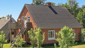 A single-story brick house with a sloped roof, a wooden staircase leading to a balcony, and a fenced yard with young trees. - 4 Person Holiday Home in Laeso (Læsø)