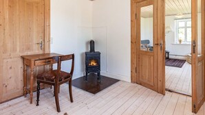 A room with a wooden door, a small wooden table, a chair, and a wood-burning stove. - 4 Person Holiday Home in Laeso (L æsø)