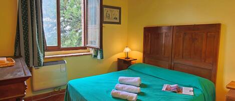 A room with a bed, a window with curtains, a nightstand with a lamp, and a radiator.