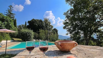 Uma mesa de pedra com duas taças de vinho, um pote de barro e várias maçãs.
