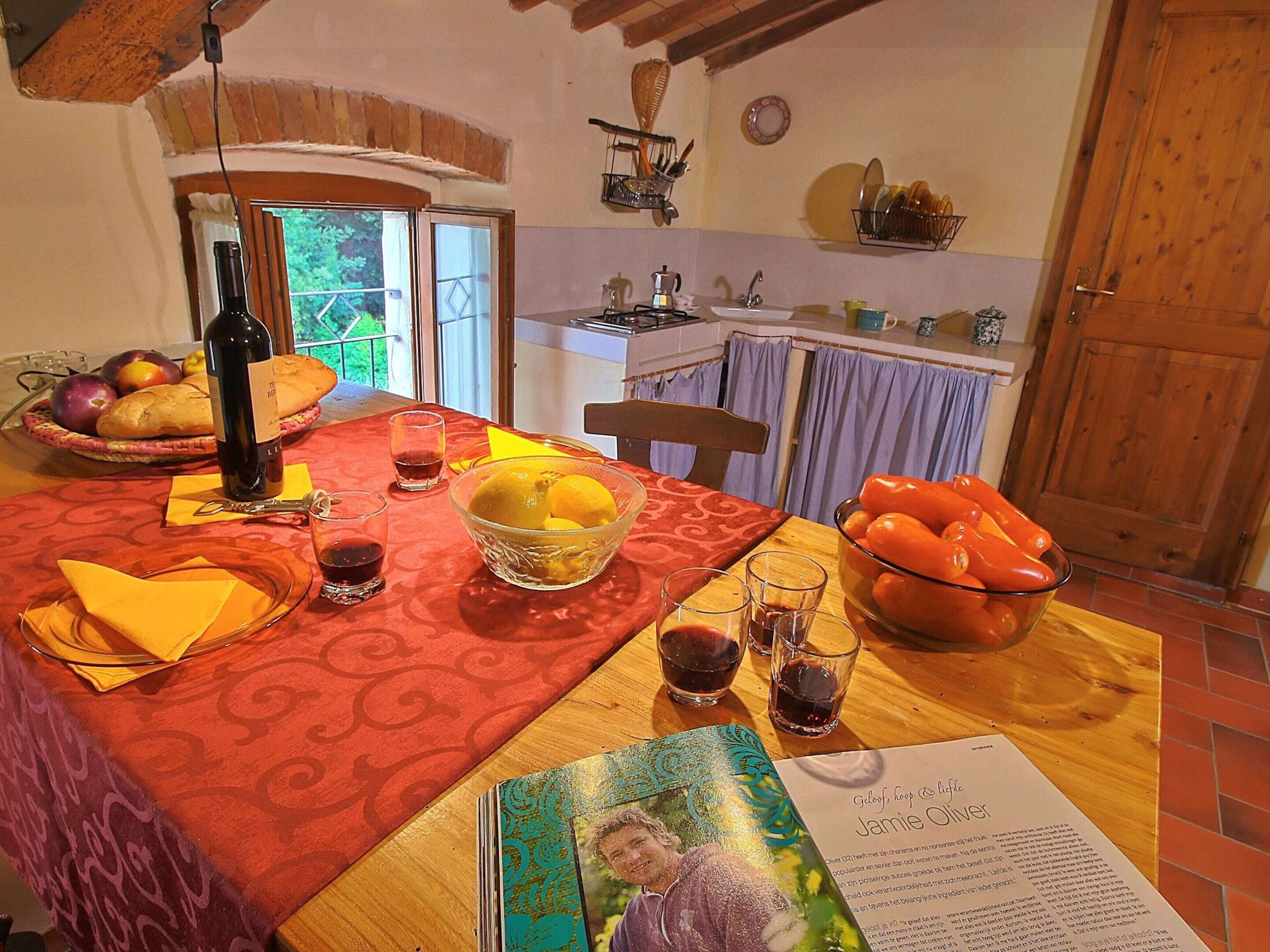 Een eettafel met een rode tafelkleed, een fles wijn, glazen, een schaal fruit en een menukaart.