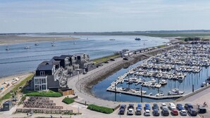 Un port de plaisance avec des bateaux amarrés, une plage où se trouvent des gens, et un bâtiment au design moderne.