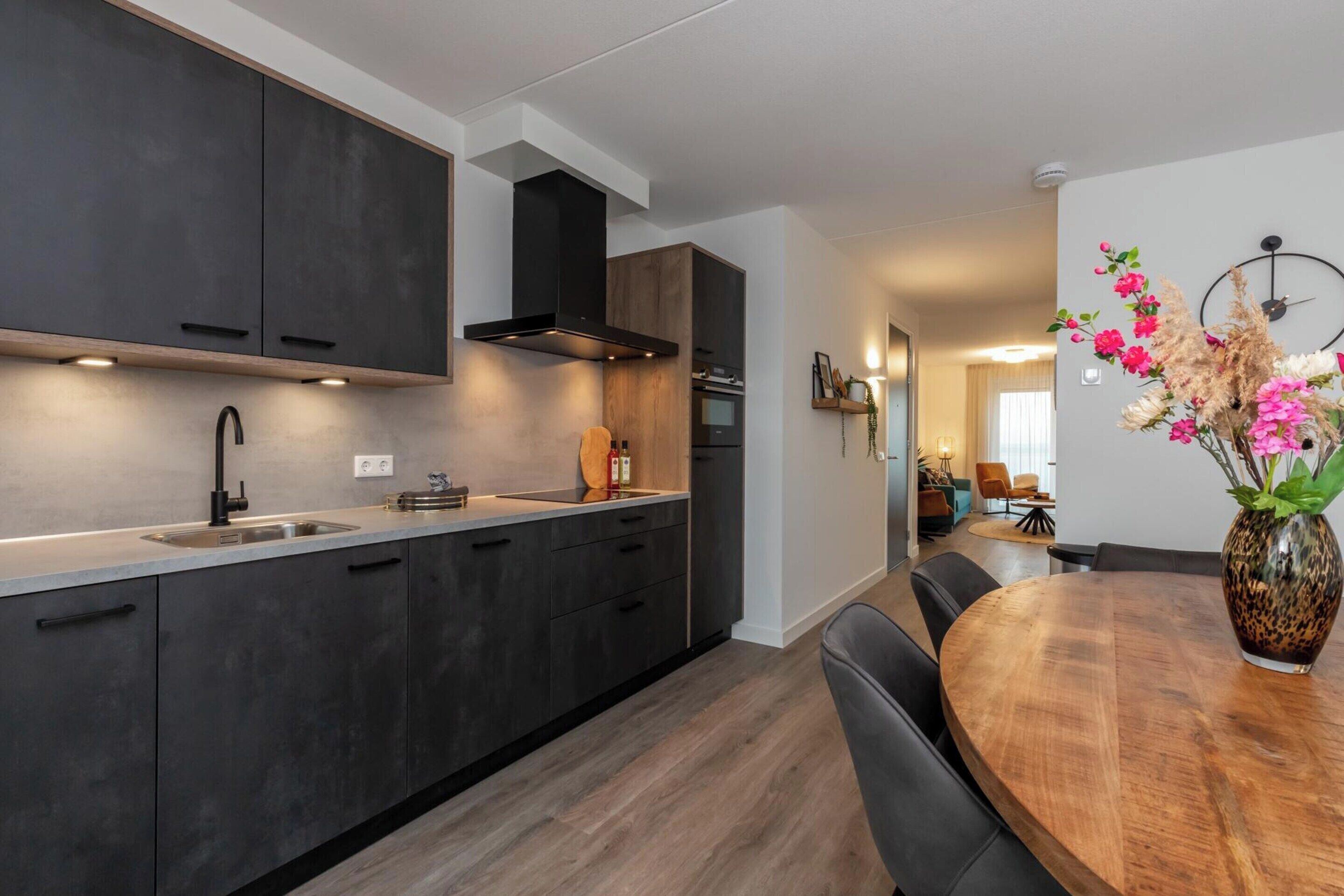 A modern kitchen with dark cabinetry, a wooden dining table, and a vase with flowers.