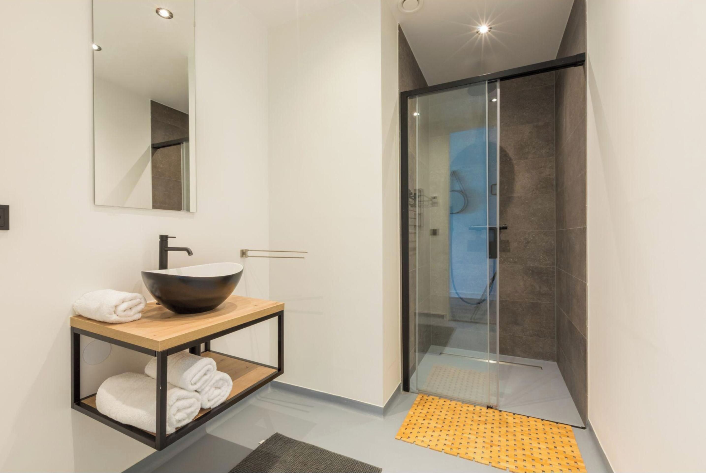 Een moderne badkamer met een grote spiegel, een wastafel op standaard, een houten wastafelmeubel en een douchecabine met glazen wanden.