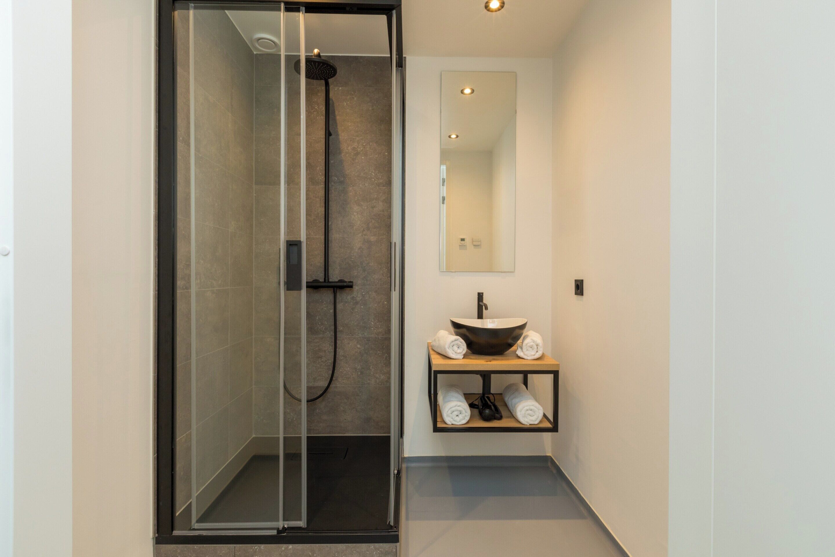 A modern bathroom with a glass-enclosed shower, a vessel sink, and a mirror above the sink.
