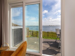A room with a sliding glass door leading to a patio with a view of the water and wind turbines. - Unique Apartment, Located on the Oosterschelde and Marina of Sint Annaland (Sint-Annaland)