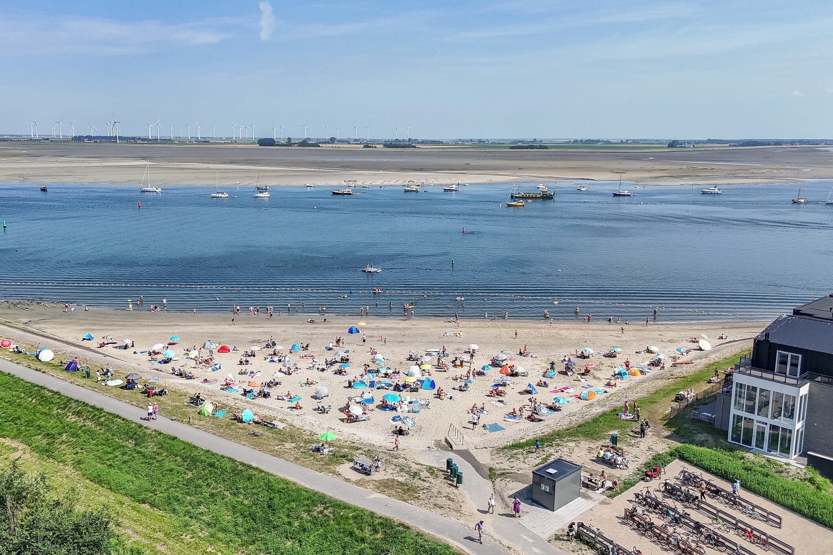 A beach with tents and people, a sandy shore, and boats in the water.