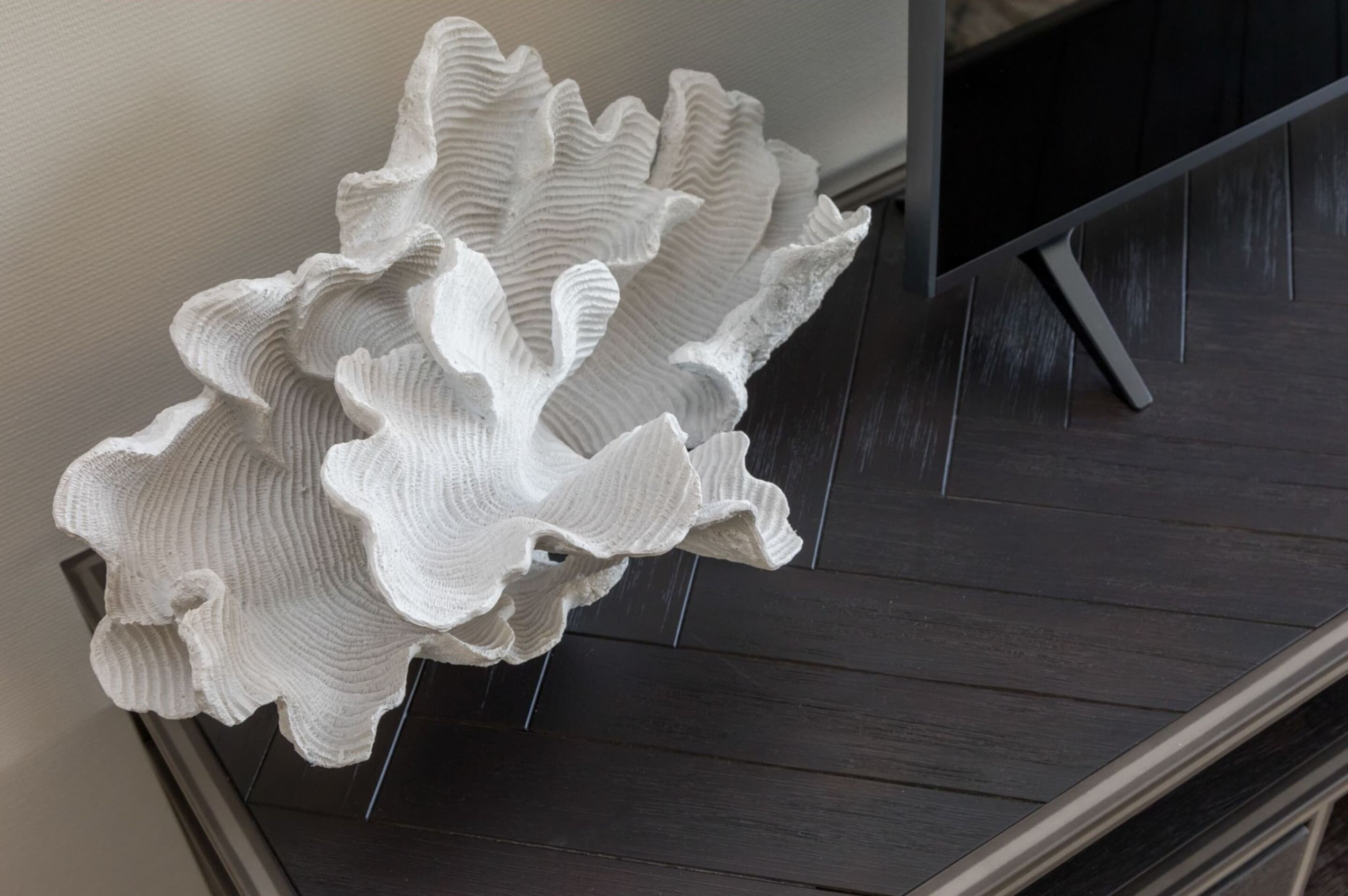 Una scultura bianca e strutturata su un pavimento in legno scuro.