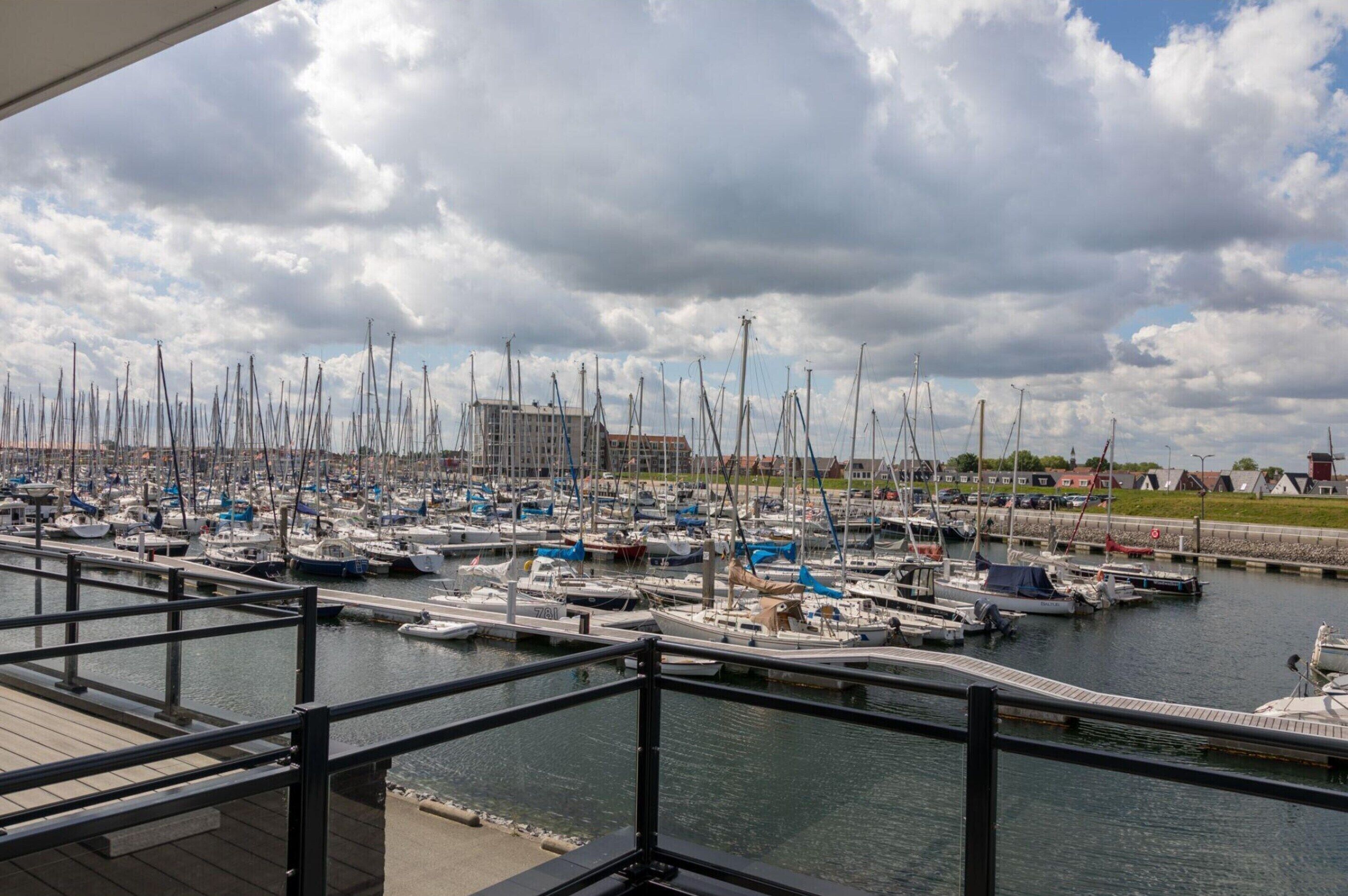 A marina with numerous boats docked, a building in the background, and a cloudy sky.