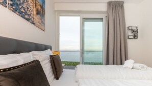 Une chambre d’hôtel avec un lit, un canapé, une grande fenêtre donnant sur la mer et un tableau accroché au mur.