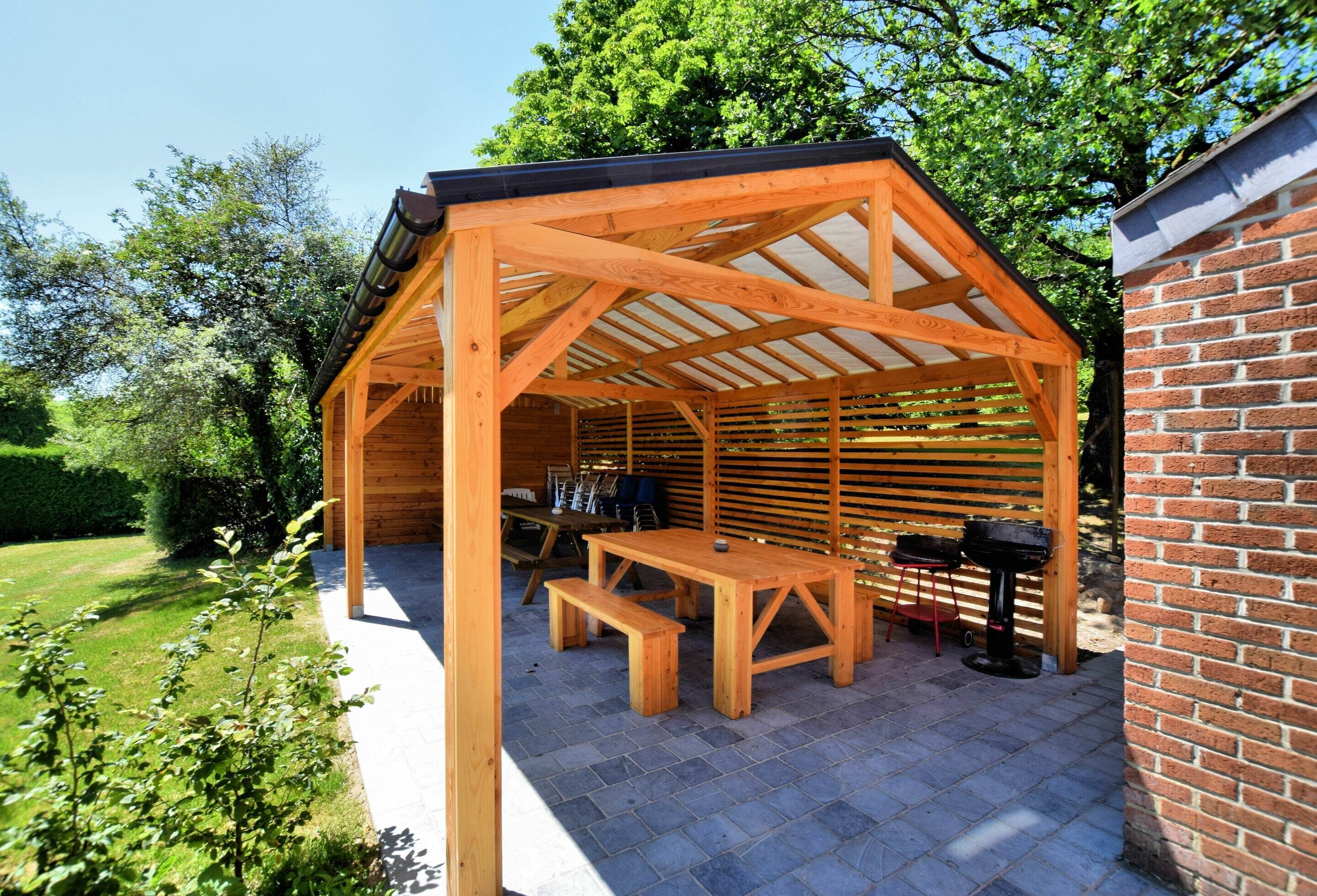 Een houten pergola met een tafel en banken, omringd door een bakstenen muur en een tuin.