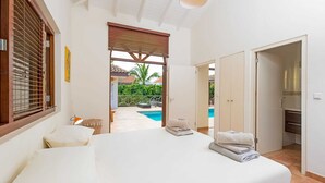 Ein Schlafzimmer mit einem großen Bett, Blick auf einen Swimmingpool und einer Tür zum Badezimmer.