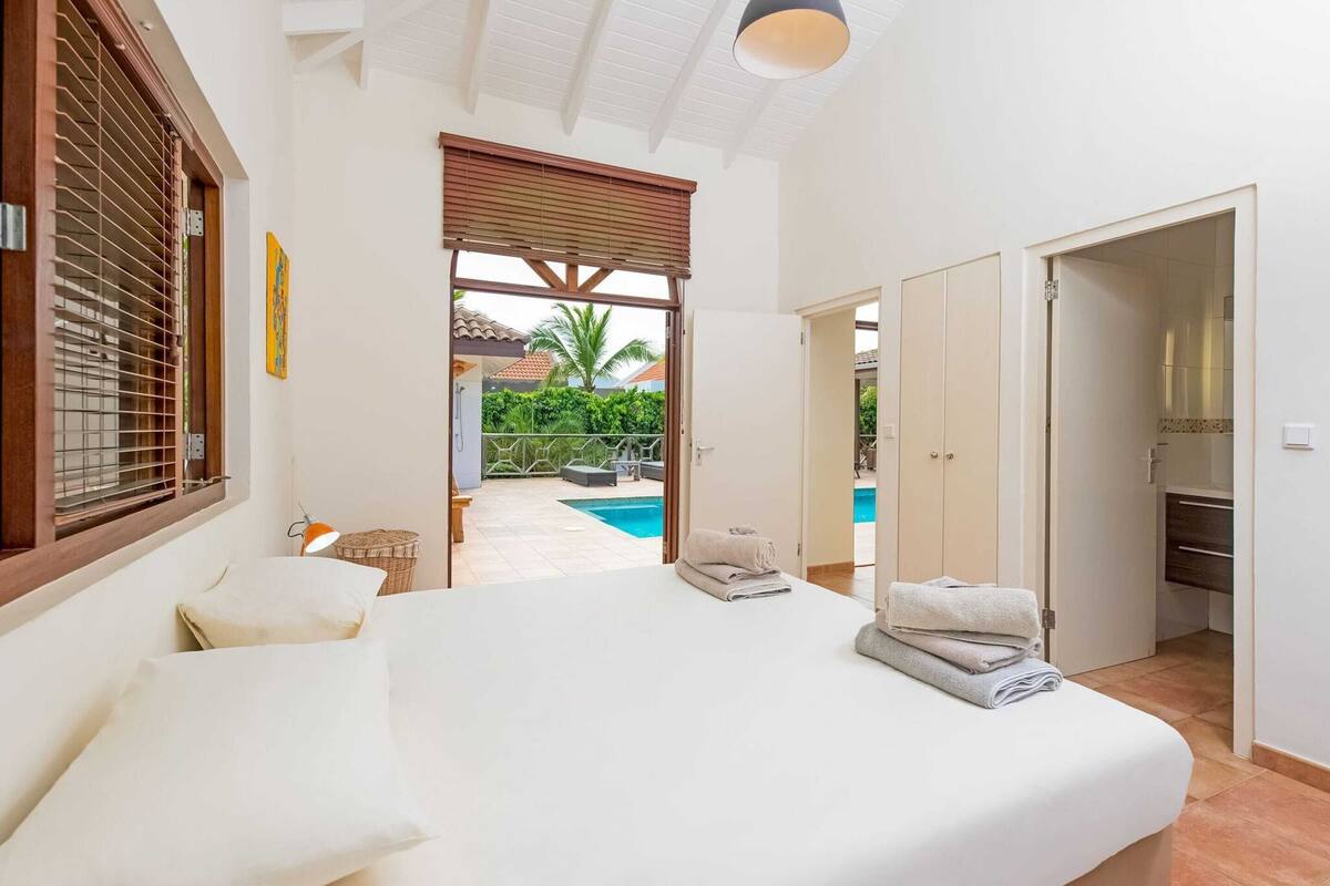 A bedroom with a large bed, a view of a swimming pool, and a door leading to a bathroom.